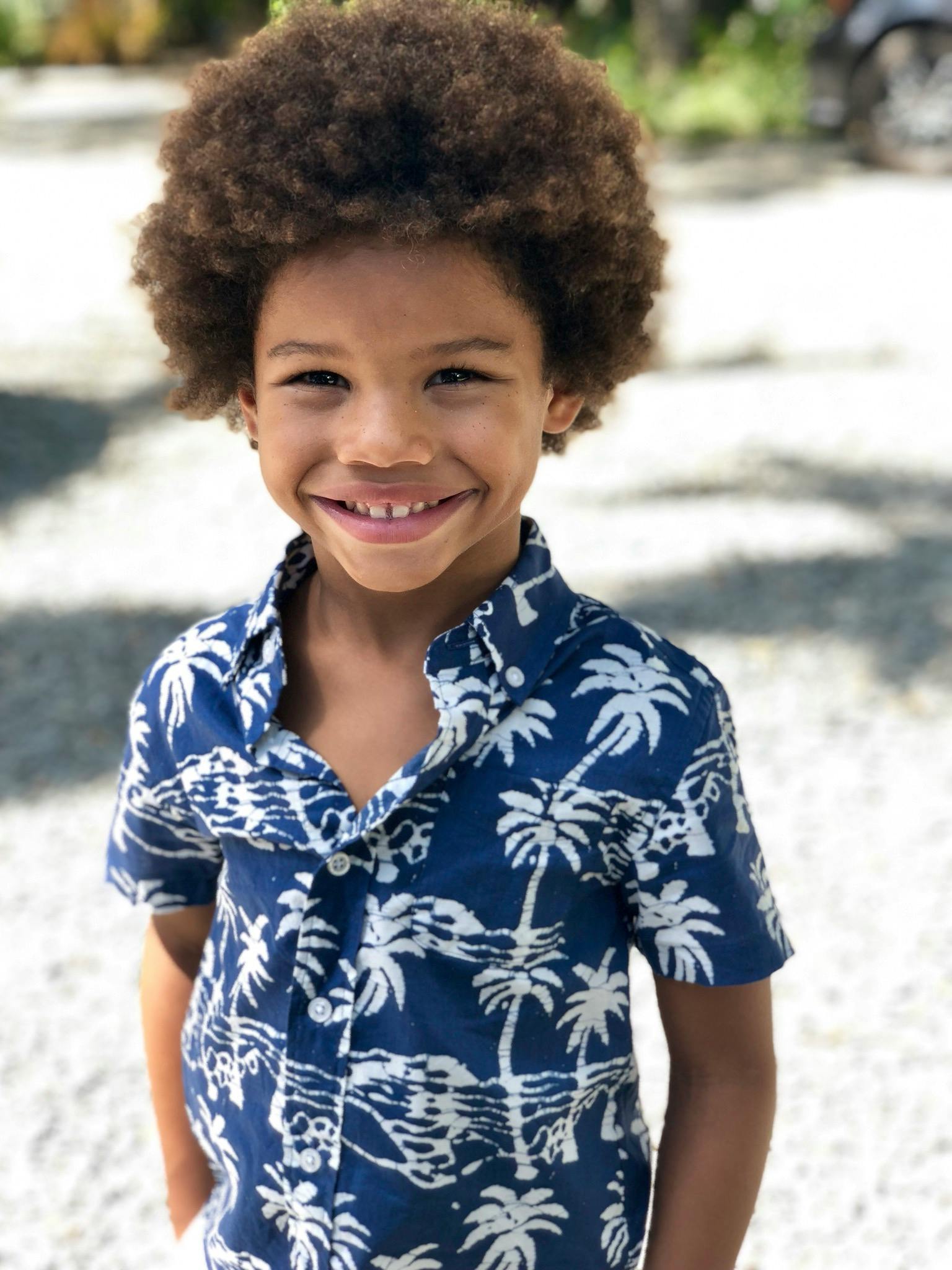 Adorable young boy with an afro smiling brightly outdoors on a sunny day.